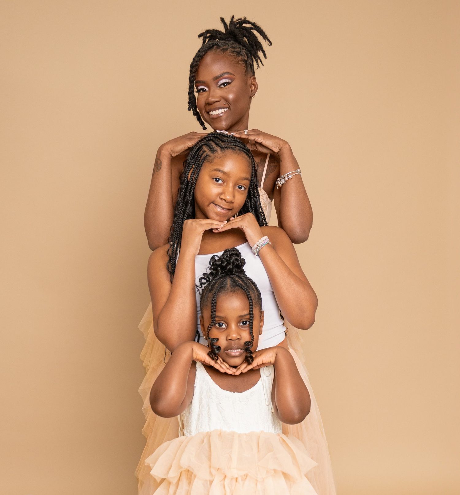 Three people in matching white outfits strike similar playful poses while standing in a vertical line against beige background.