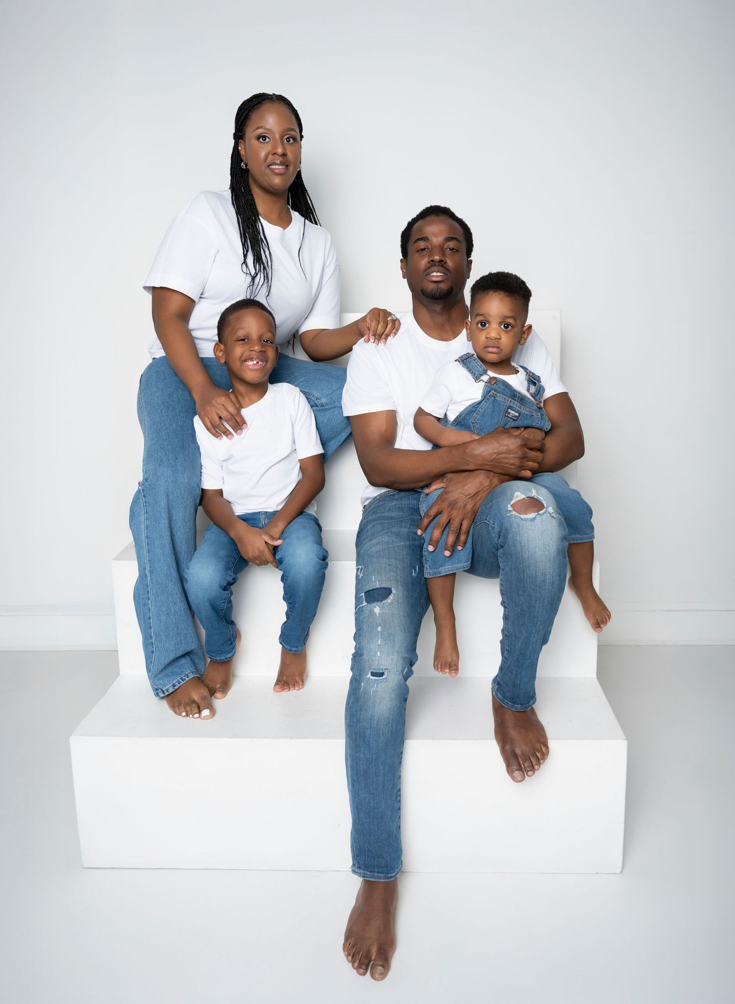 Family members wearing white shirts and jeans sit together on white steps in a series of candid studio portraits.