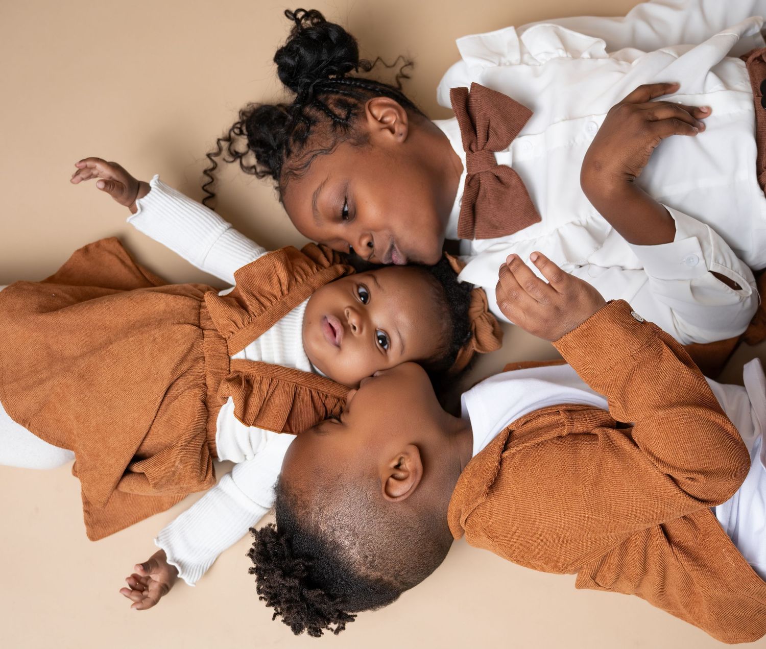 Three babies dressed in brown and white clothing sleeping together on a soft white surface.
