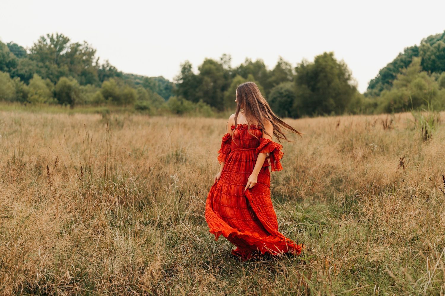Woman in red dress spinning gracefully in a rustic field at golden hour. rockford il family photographer senior photoshoot