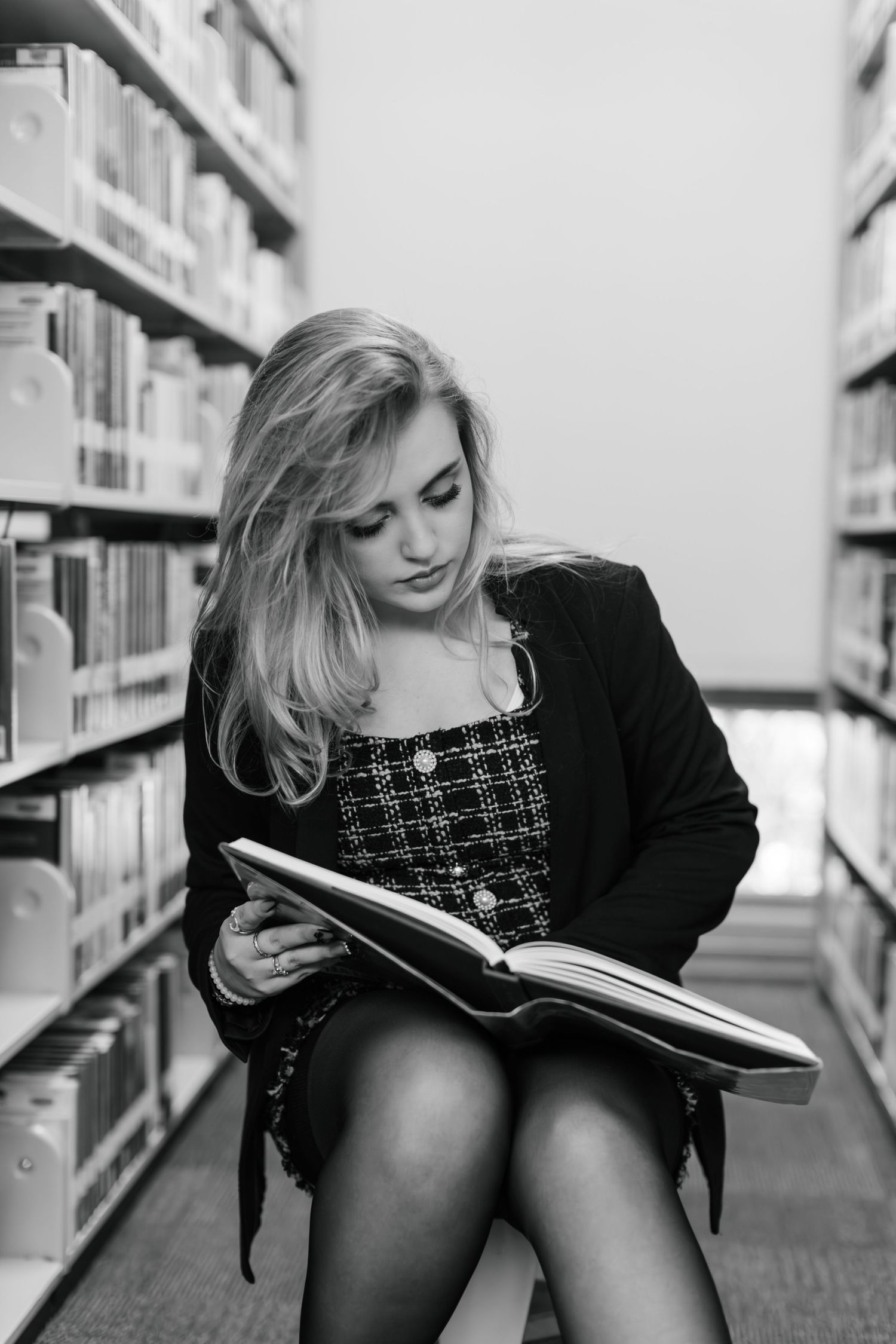 Black and white photo of someone reading a book between library shelves while sitting on the floor.