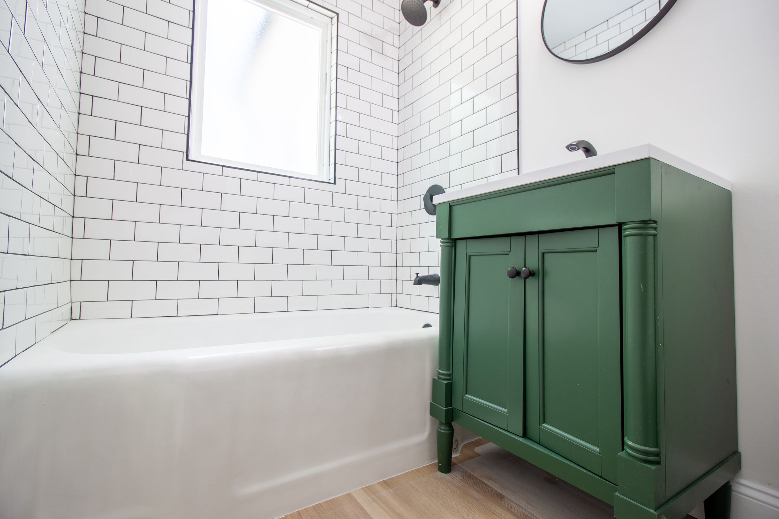 Modern and trendy updated bathroom with simple finishes. Green sink vanity and plain white subway tile with dark grout. Light colored floors