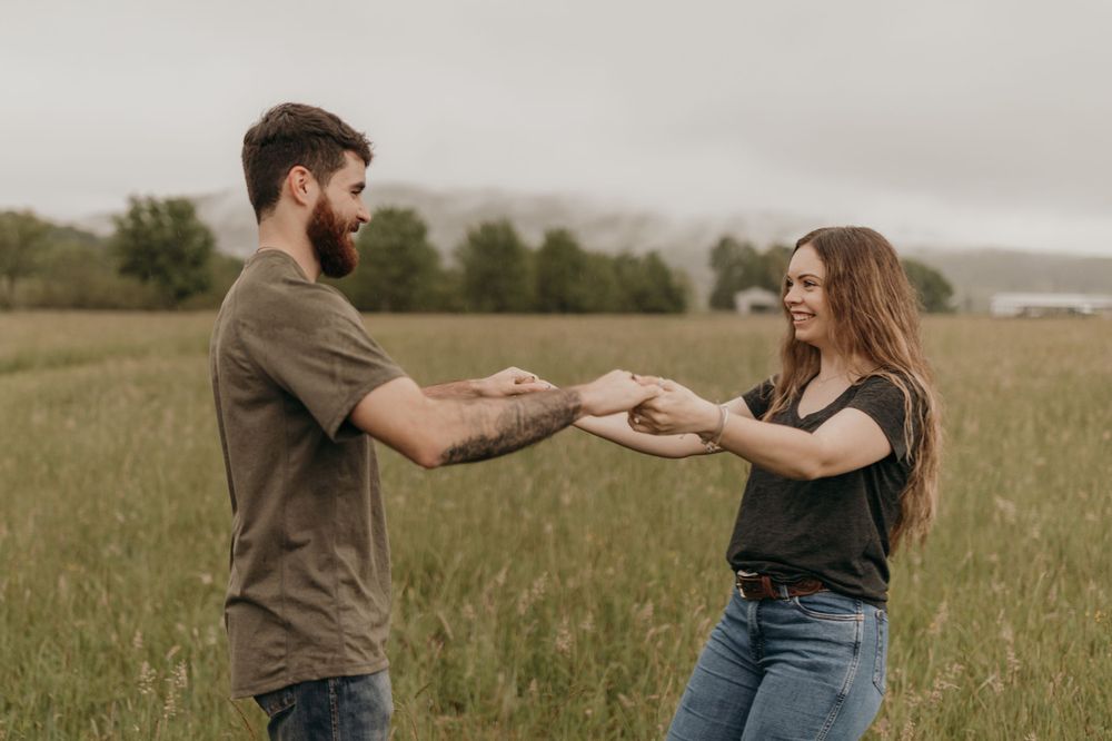 A couple holds hands while standing together in a grassy field on an rainy, overcast day.