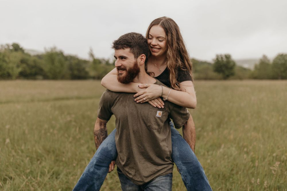 A piggyback ride moment captured in a field with during a rainy engagement session.