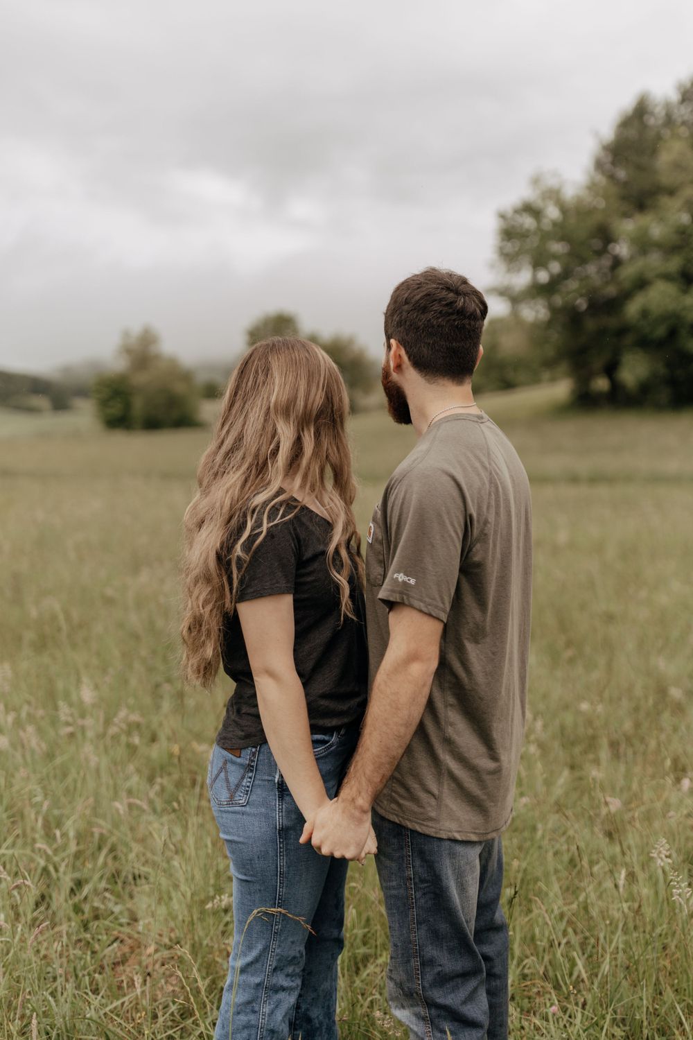 A couple stands holding hands in a misty field on an overcast day.