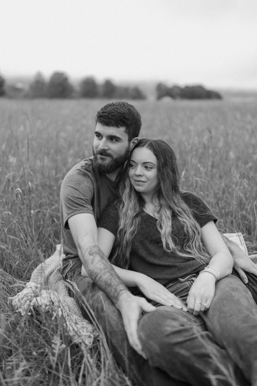 A black and white portrait of an engaged couple sitting together in a peaceful field.