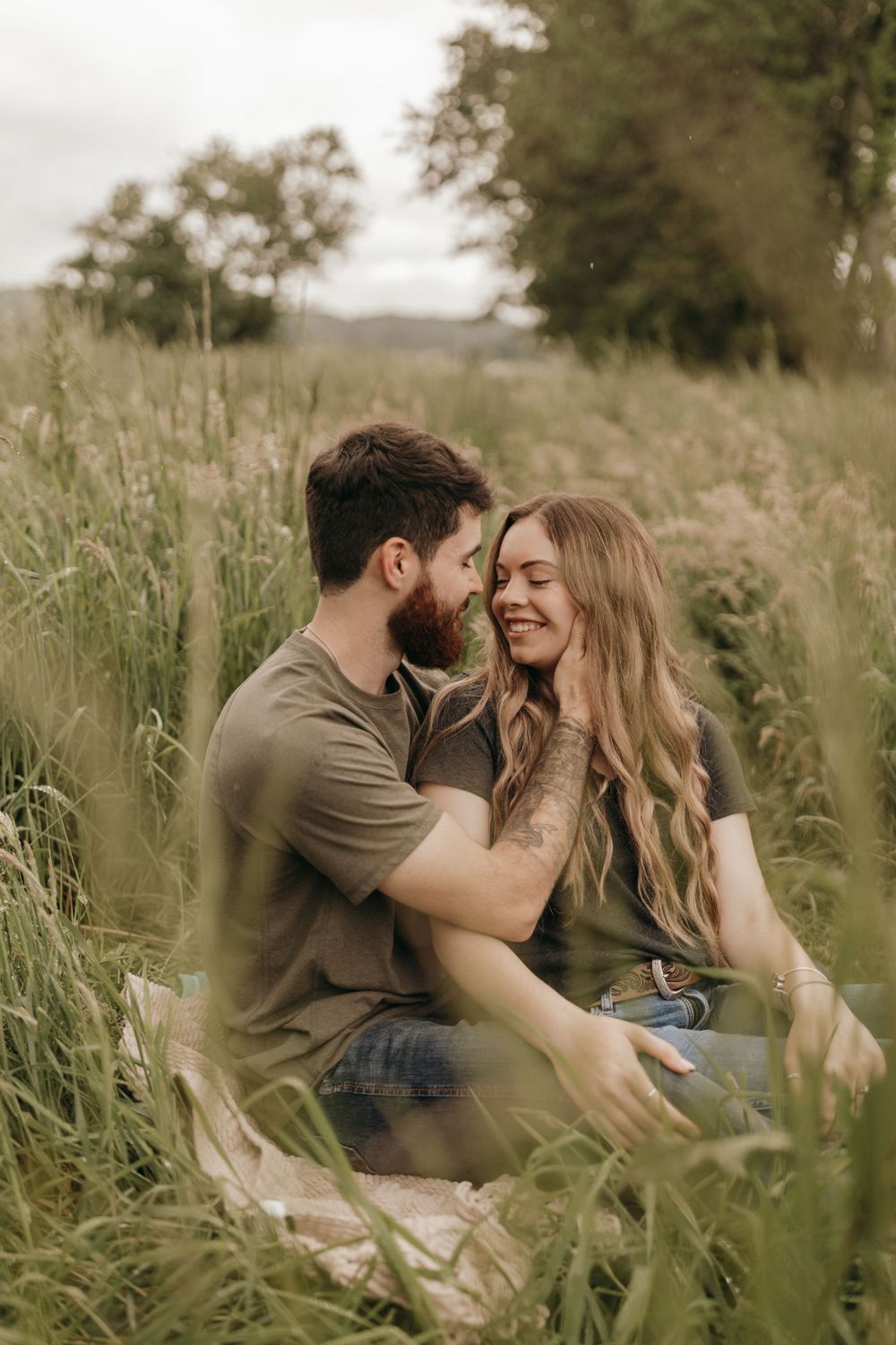 A couple shares a tender moment while sitting in tall grass during sunset.