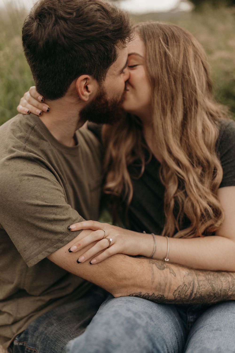 A couple shares a romantic kiss while sitting in a grassy field.