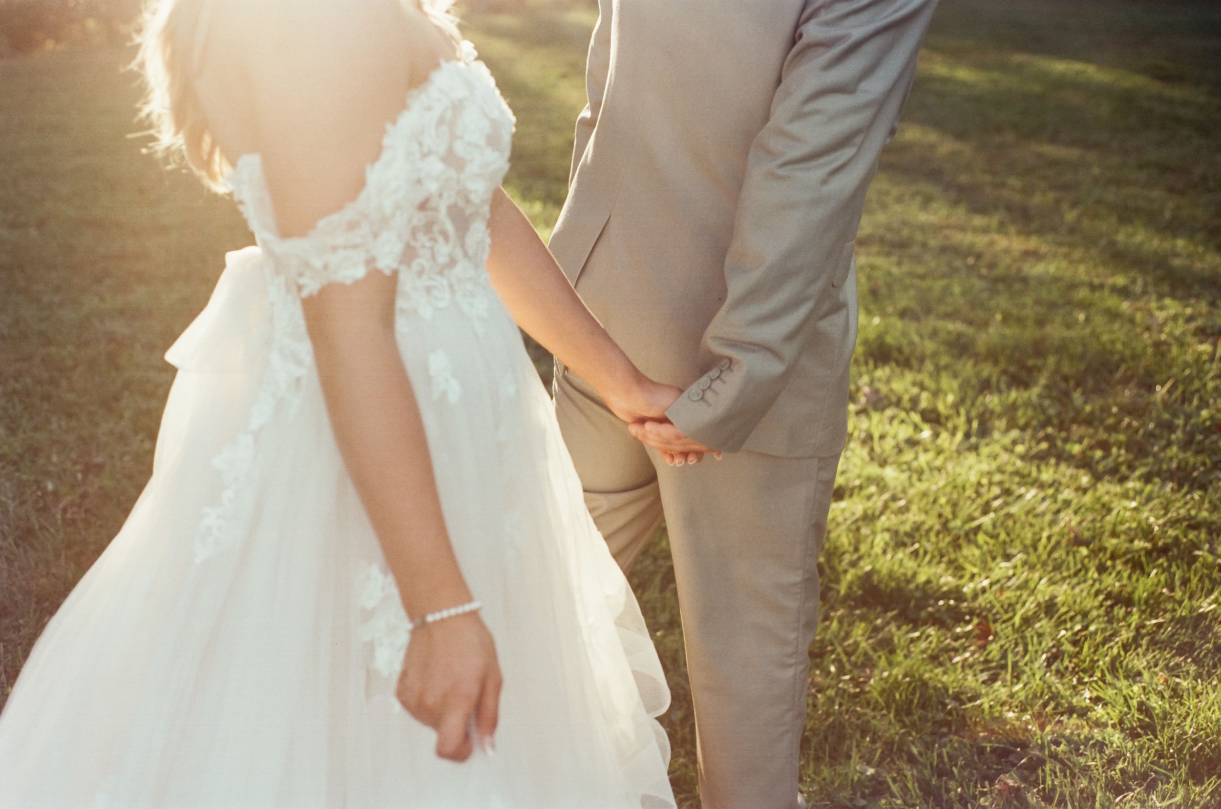 Romantic sunlit wedding photography showing dress details and clasped hands.