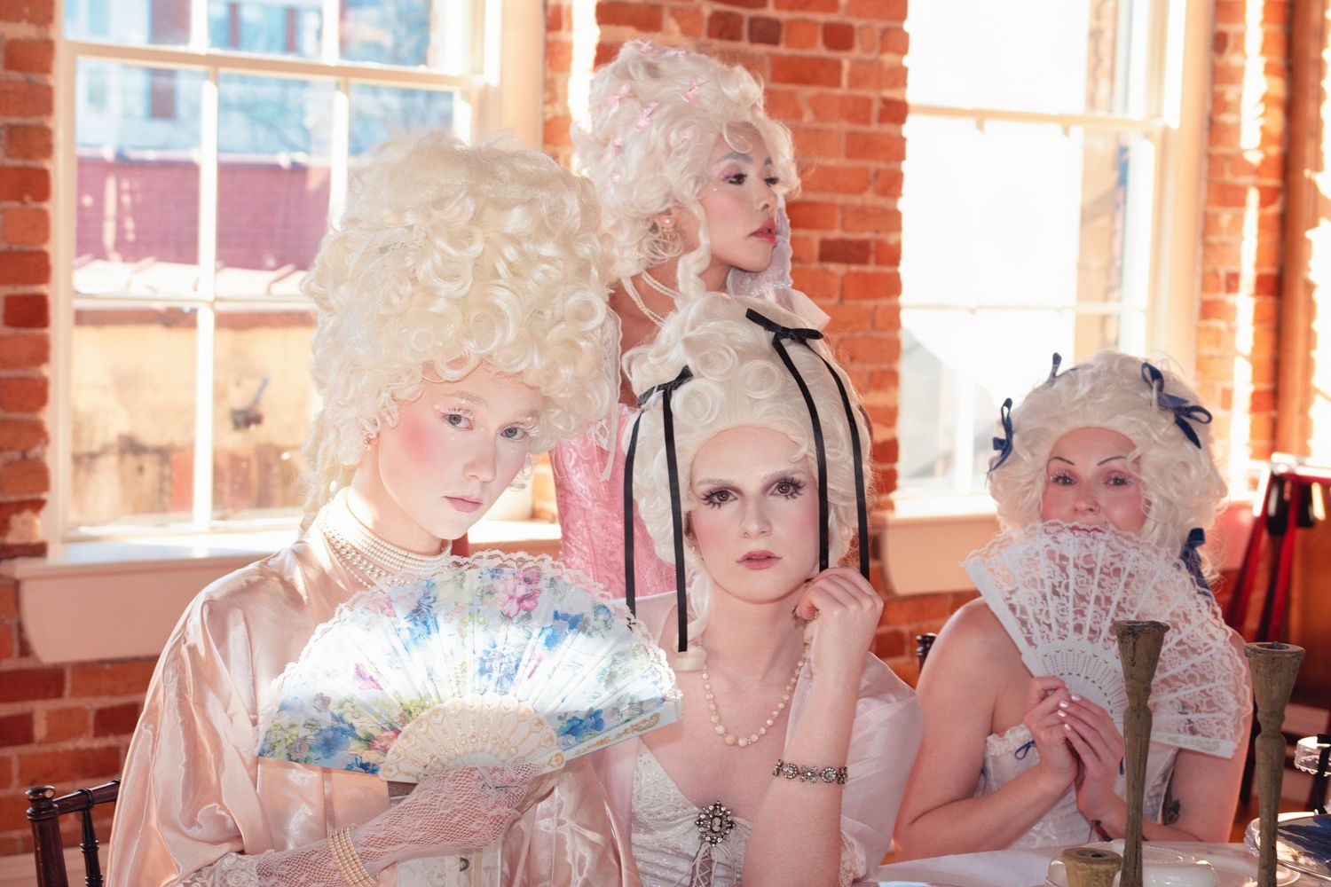 Three people in vintage Victorian style costumes with white wigs posing in a historic brick room.