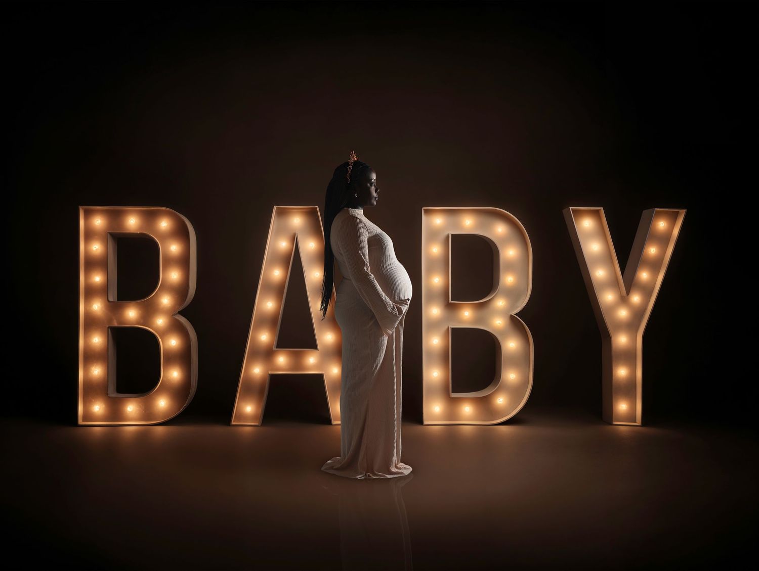 A silhouetted figure stands in front of illuminated marquee letters spelling BABY against a dark background.