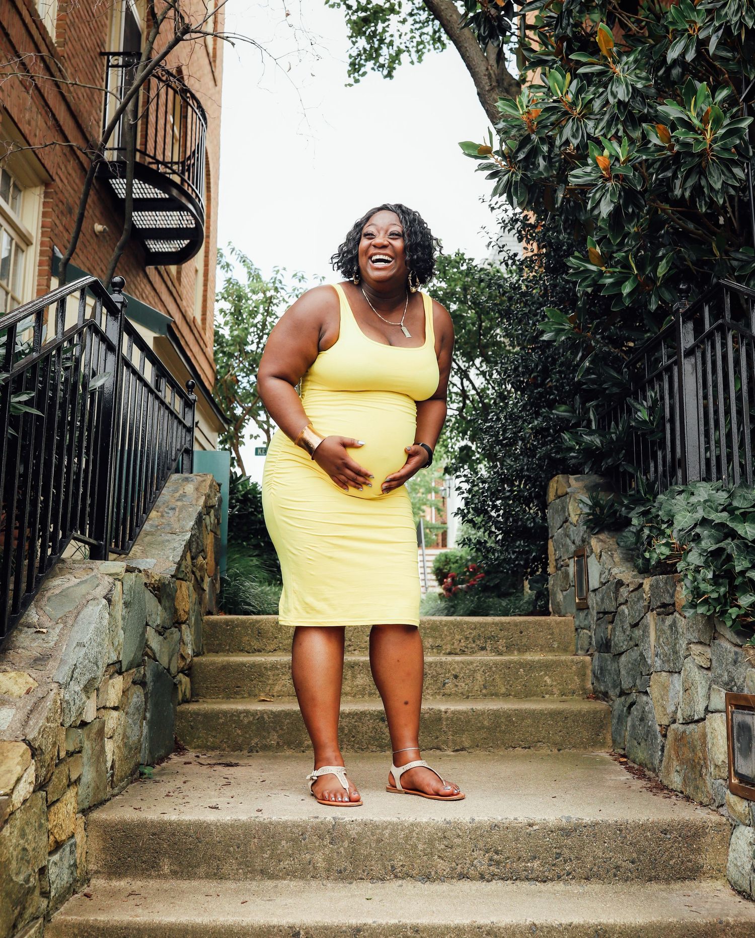 A summertime maternity portrait on stone steps with yellow dress and natural surroundings.