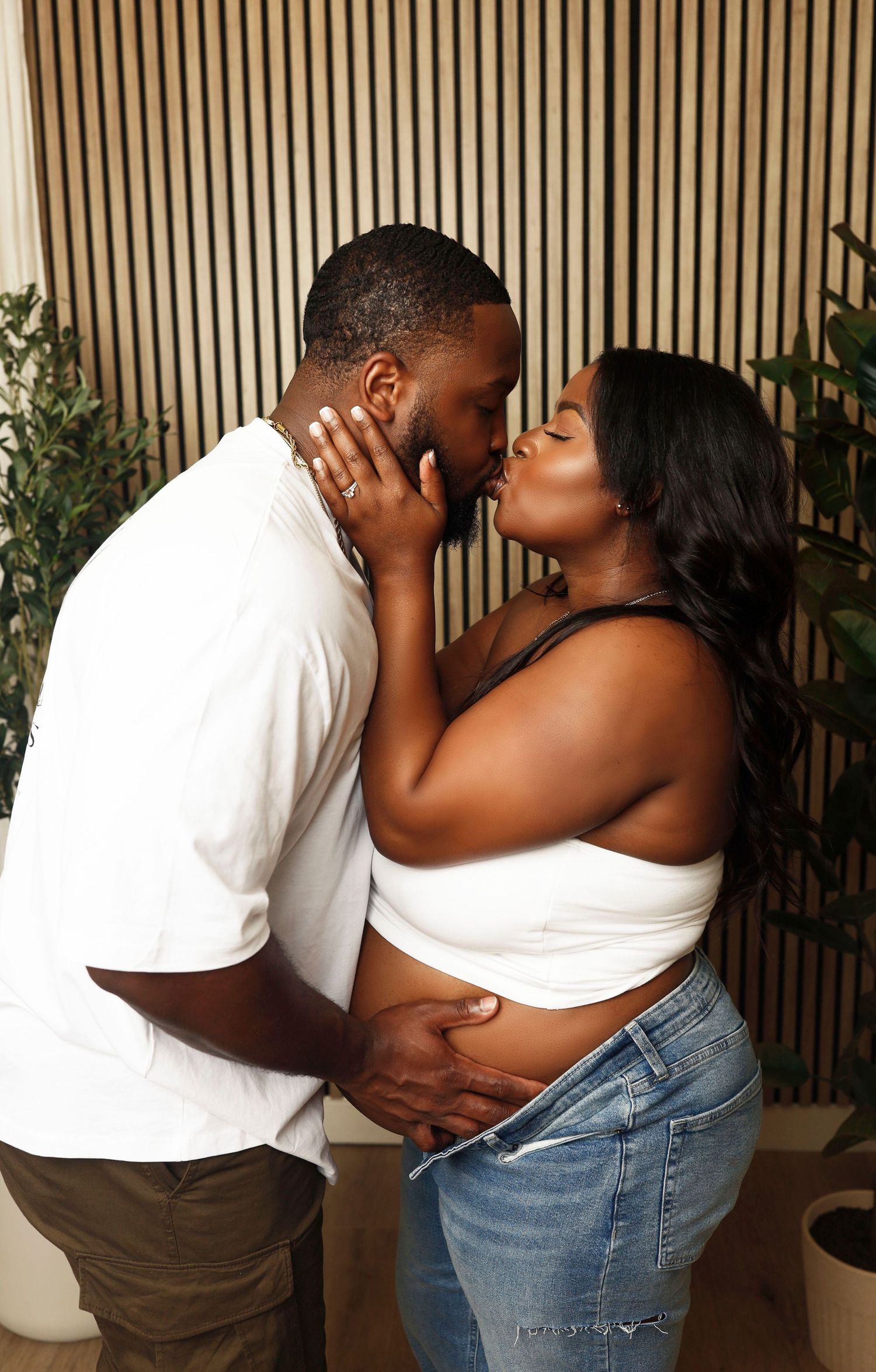 A romantic maternity photoshoot featuring a tender moment between a couple against a wooden slat background.