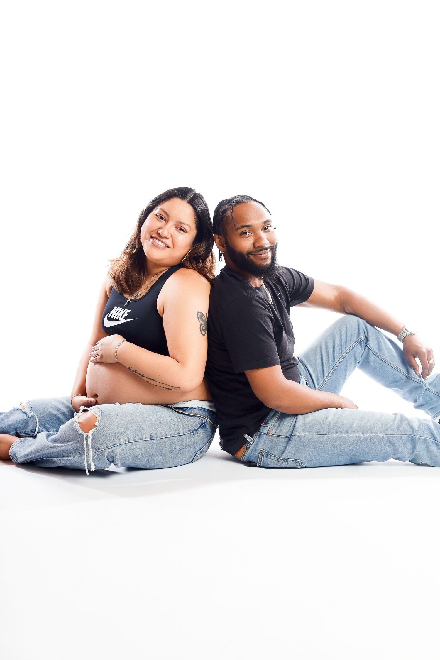 Casual couple portrait sitting back-to-back wearing jeans against white background.