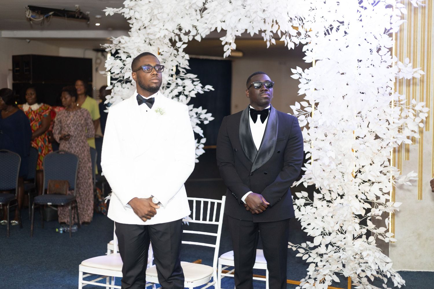 Two people stand under white floral decorations during a wedding ceremony.