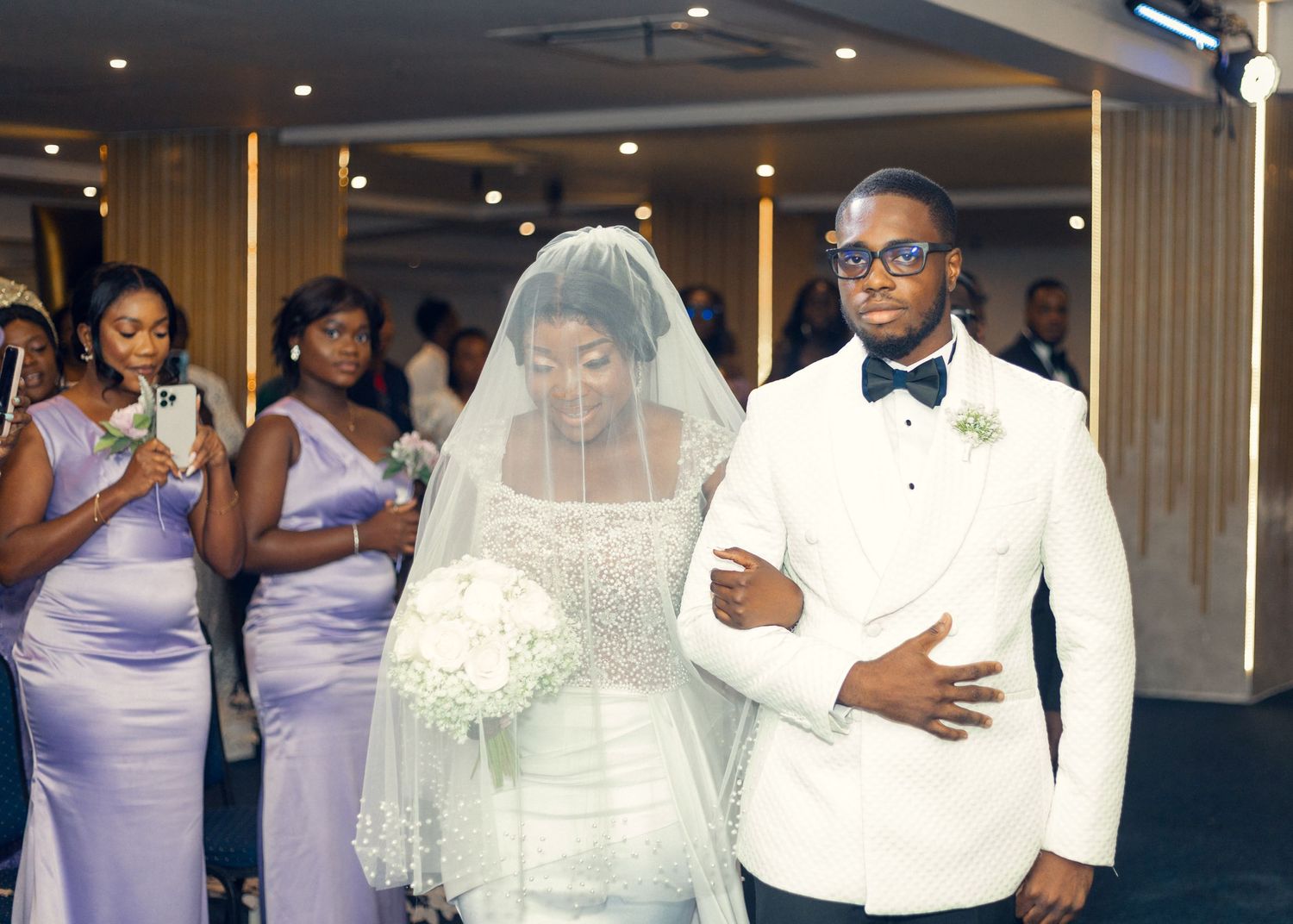 A wedding ceremony processional with bridesmaids in purple dresses watching the couple.