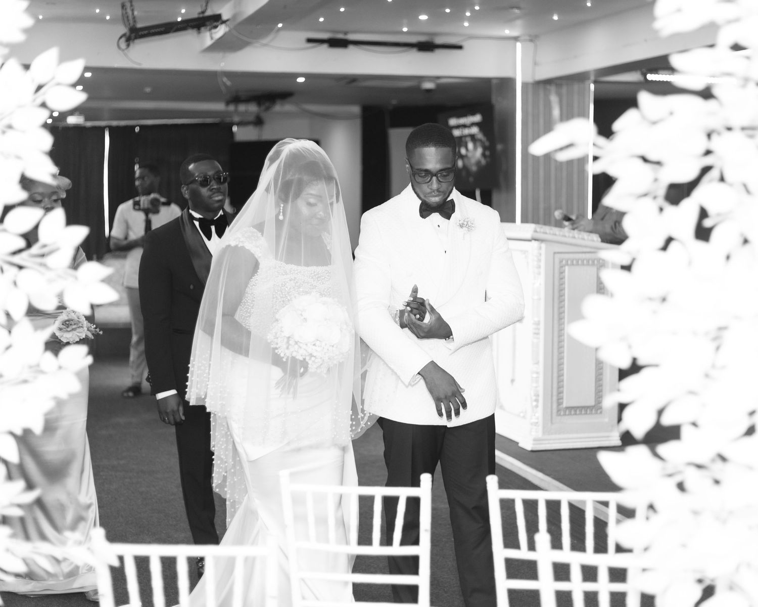 A black and white photo of a couple during their wedding ceremony with white floral decorations.