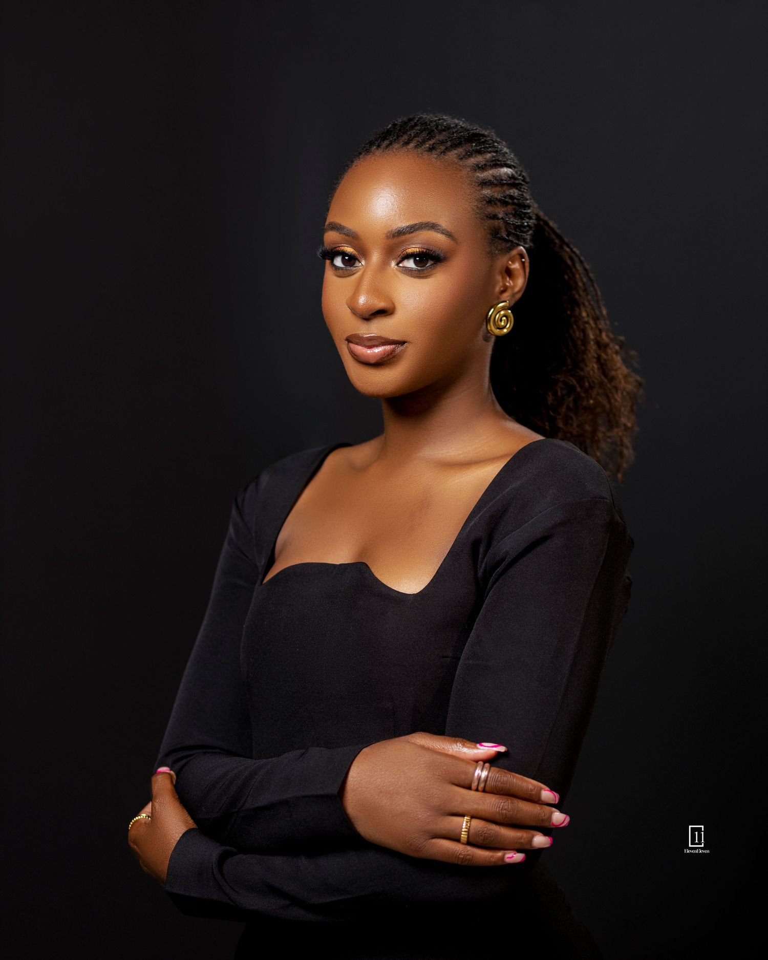 Professional studio portrait of a woman in black top with braided hair and subtle makeup against dark background.