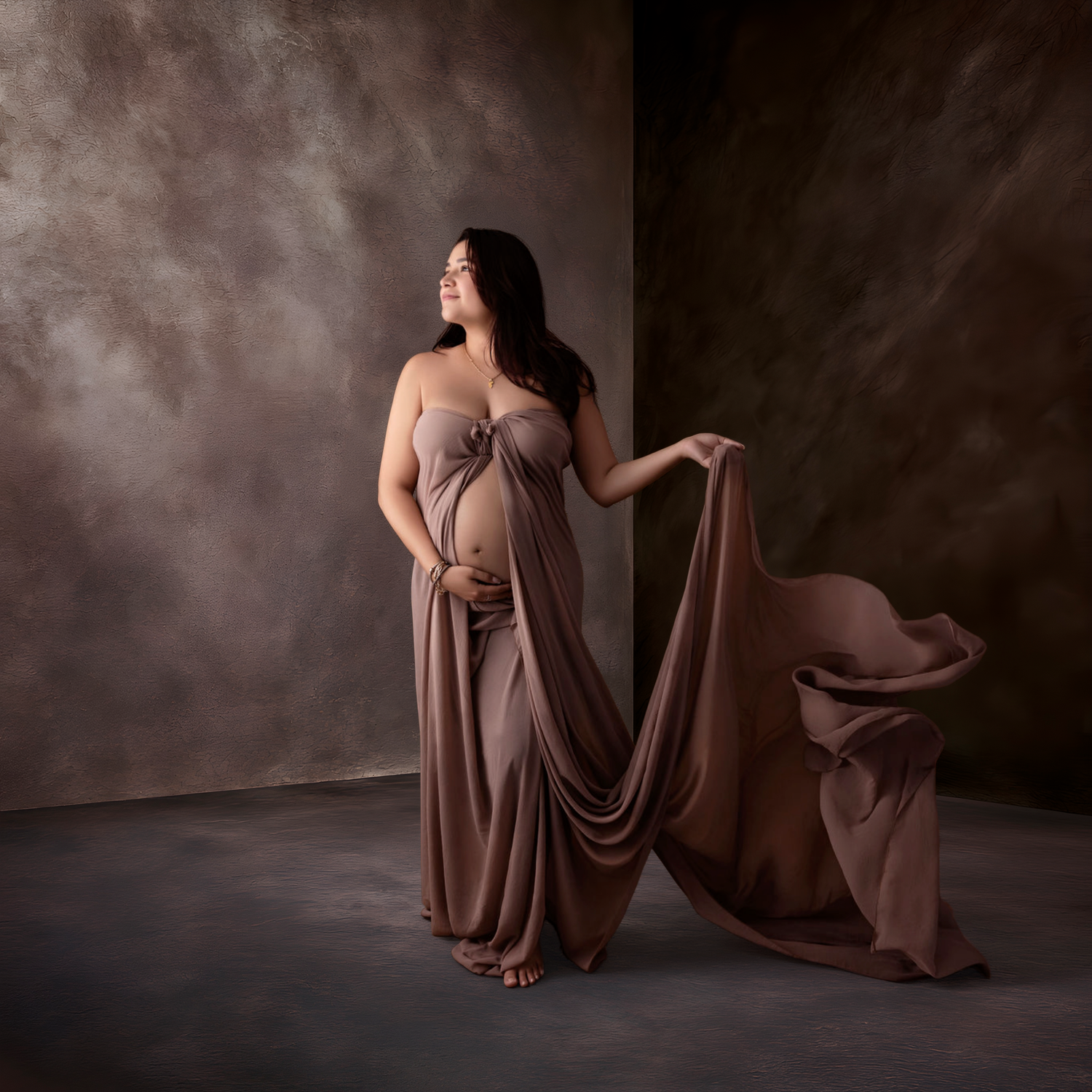 A serene maternity photo with flowing turquoise fabric against a teal background creating an ethereal effect.
