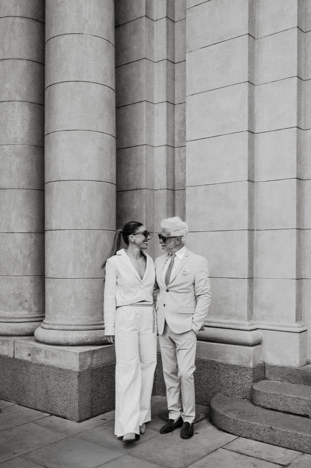 Couple standing between classical stone columns of historic building.