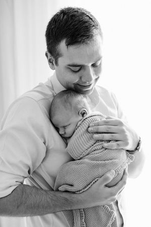 Black and white photo series showing tender moments between a parent and newborn baby in matching gingham outfits.