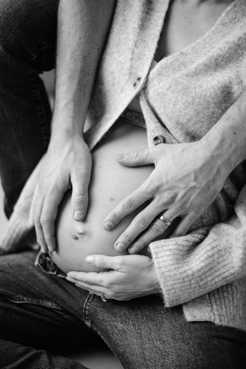 Black and white close-up of hands gently touching a pregnant belly through a sweater.