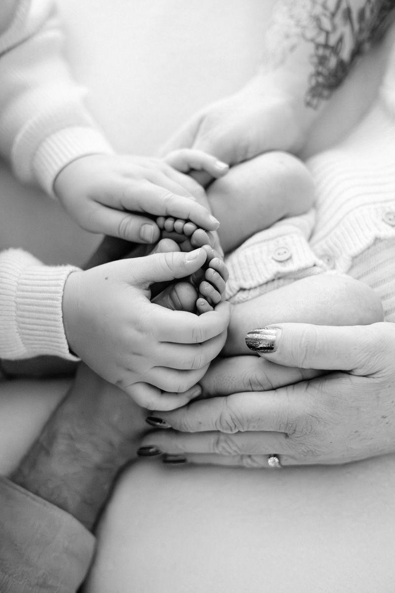 Black and white close-up of hands tenderly holding a baby's tiny feet in a heartwarming family moment.