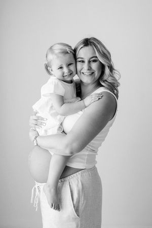 Black and white photo showing mother to be hugging her toddler on her bump at their natural light maternity shoot in nottingham