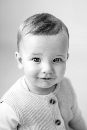 A series of black and white portraits showing a baby in a white sweater making adorable expressions.