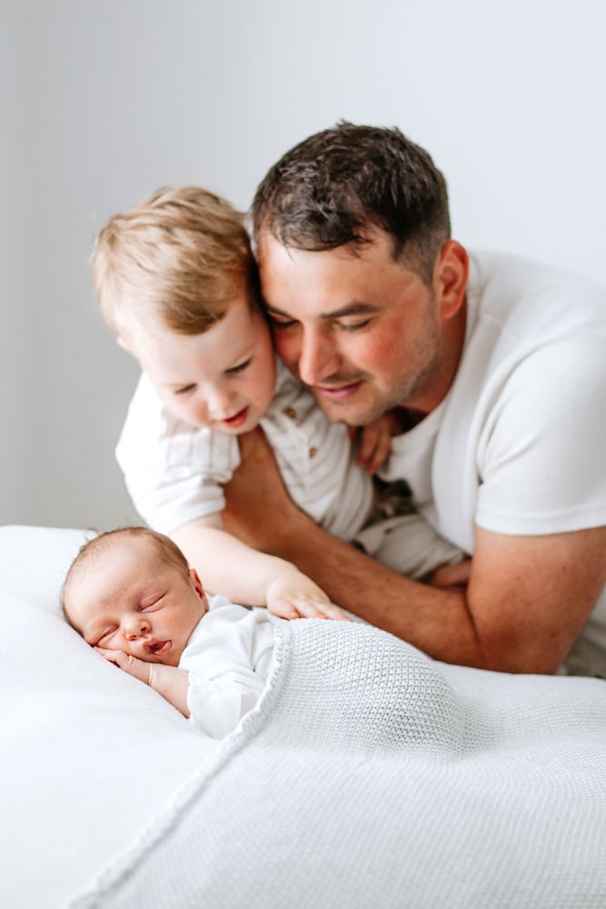 A tender moment as a parent and child gaze lovingly at a sleeping baby in white bed linens.