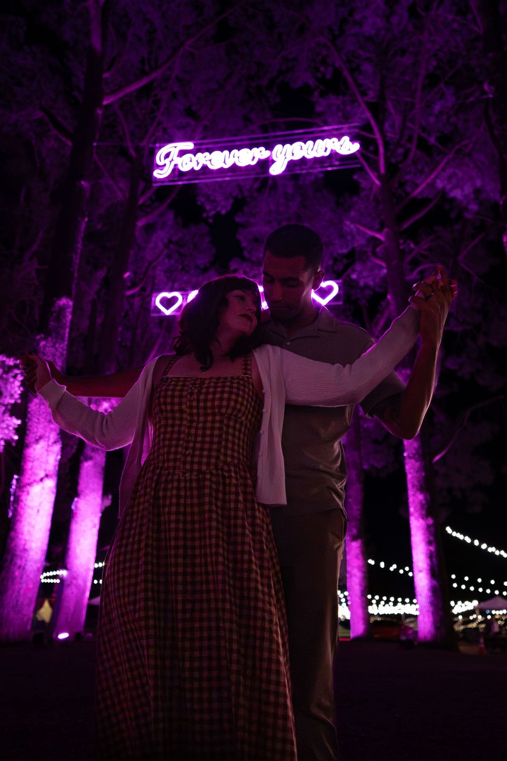 Purple-lit outdoor scene with illuminated neon 'Forever yours' sign and string lights creating a romantic ambiance.