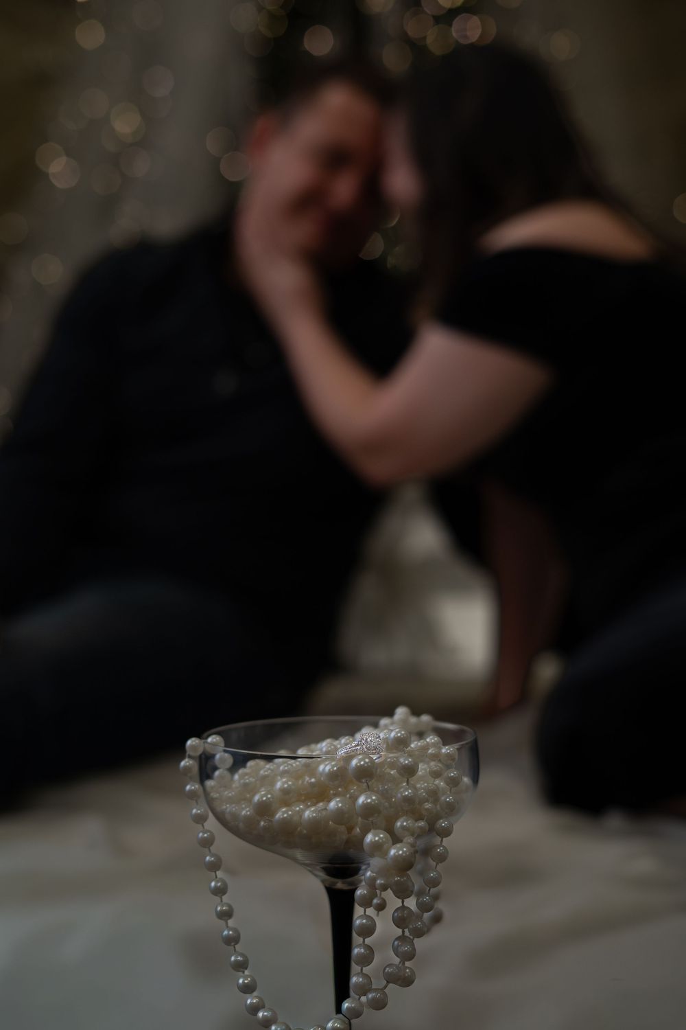 A martini glass adorned with draped pearl necklaces sits on a white tablecloth with a blurred dark background.