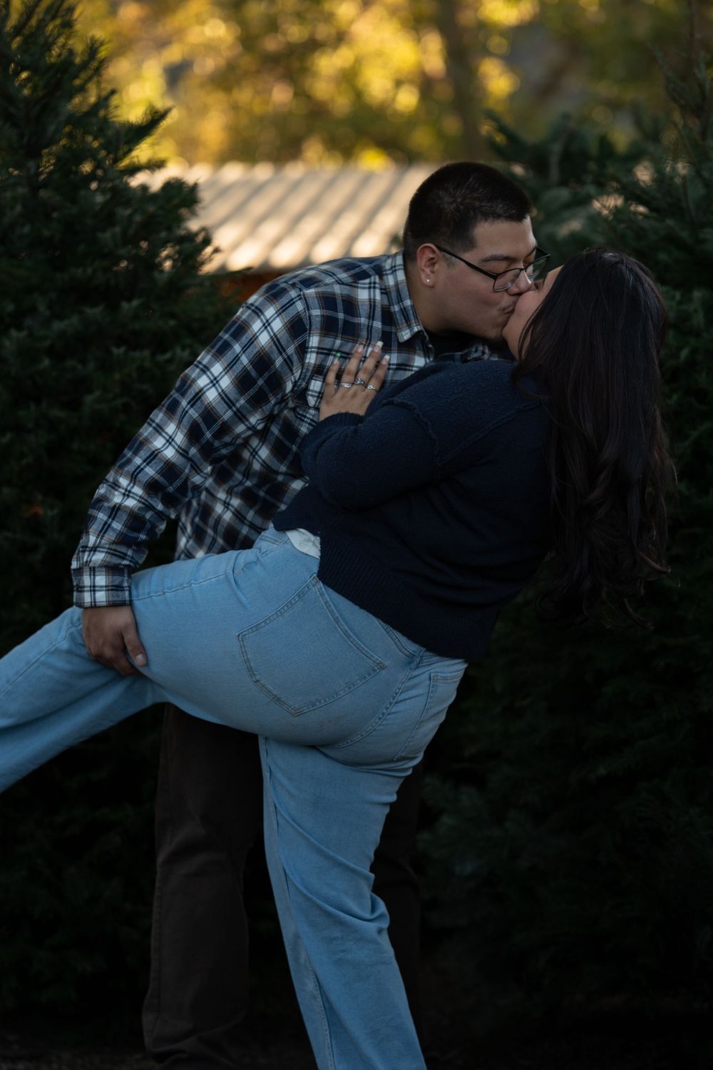 A couple in plaid and white sharing a romantic dip pose during a golden hour outdoor photoshoot.