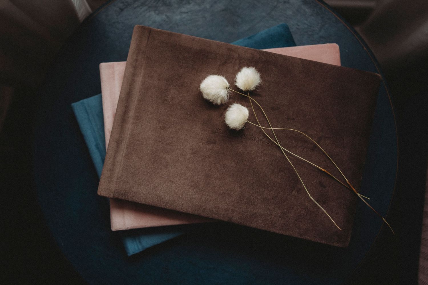 Brown velvet photo album or book stacked with blue fabric, decorated with delicate dried cotton flowers on top.