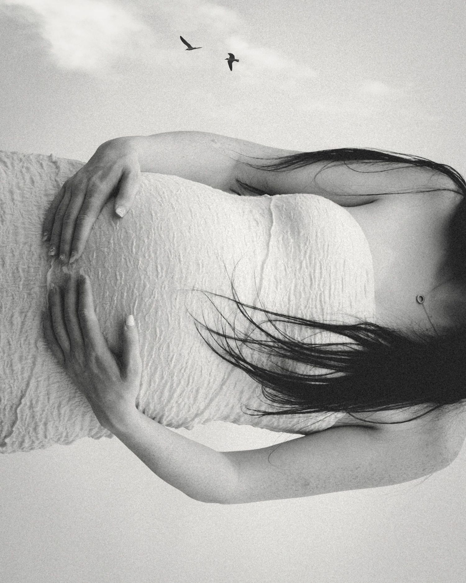 Black and white artistic photograph of a bare back with dark hair against white background as birds fly overhead.
