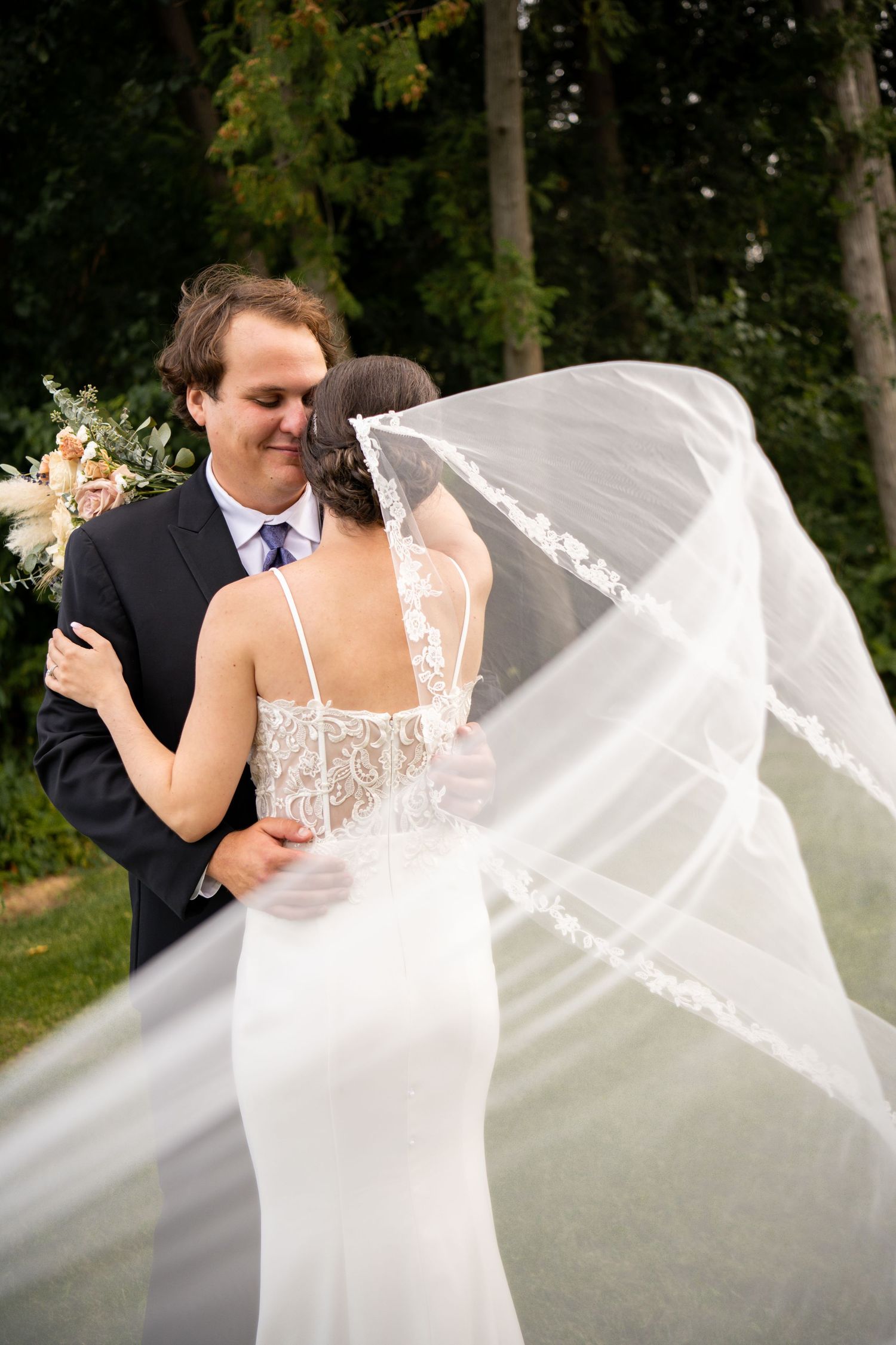 Wedding couple embracing outdoors as bride's veil flows dramatically in the wind.