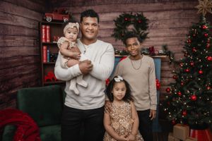 A warm family holiday portrait in front of a decorated Christmas tree with rustic wood wall background.