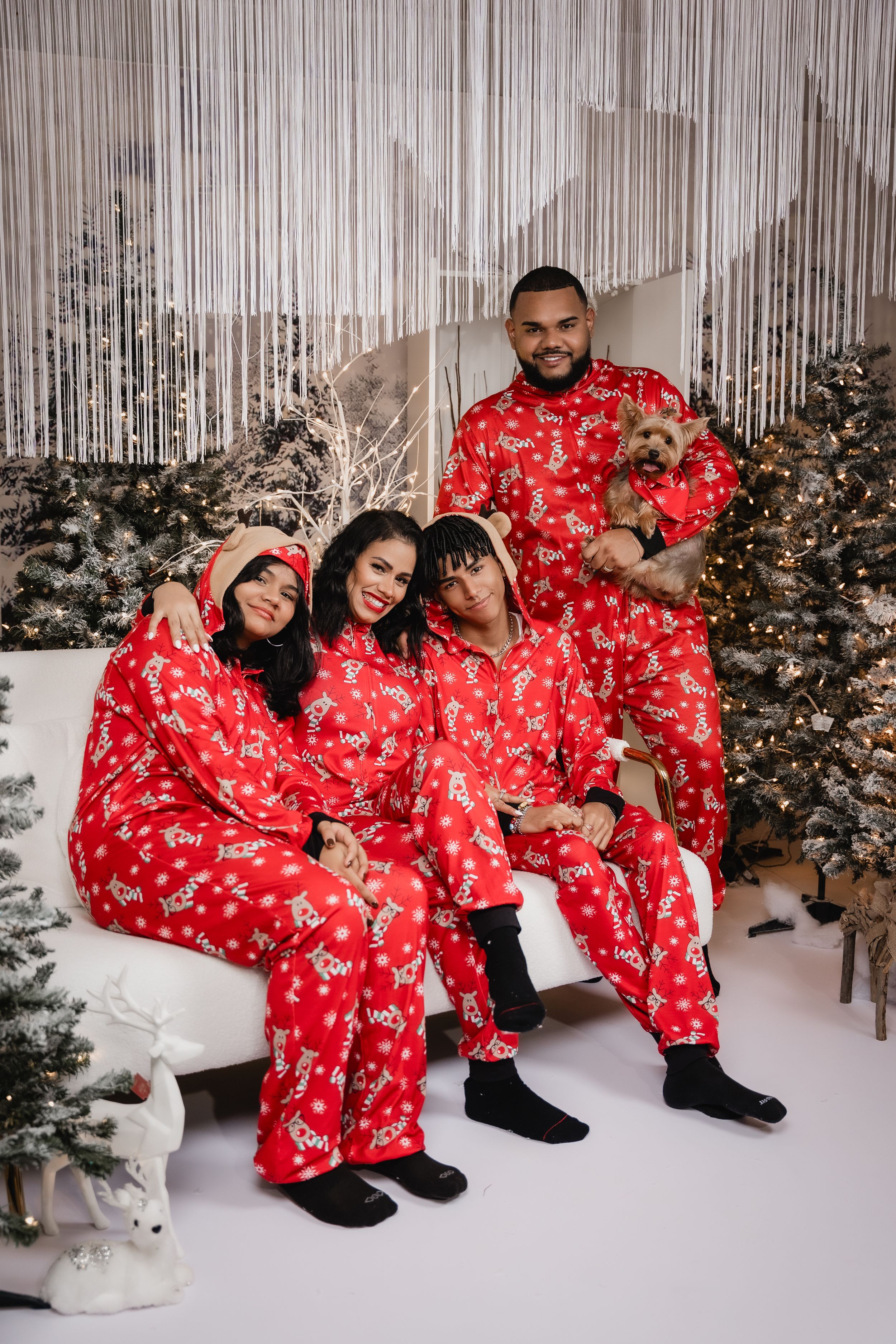 A family wearing matching red holiday pajamas poses together on a couch with their dog.
