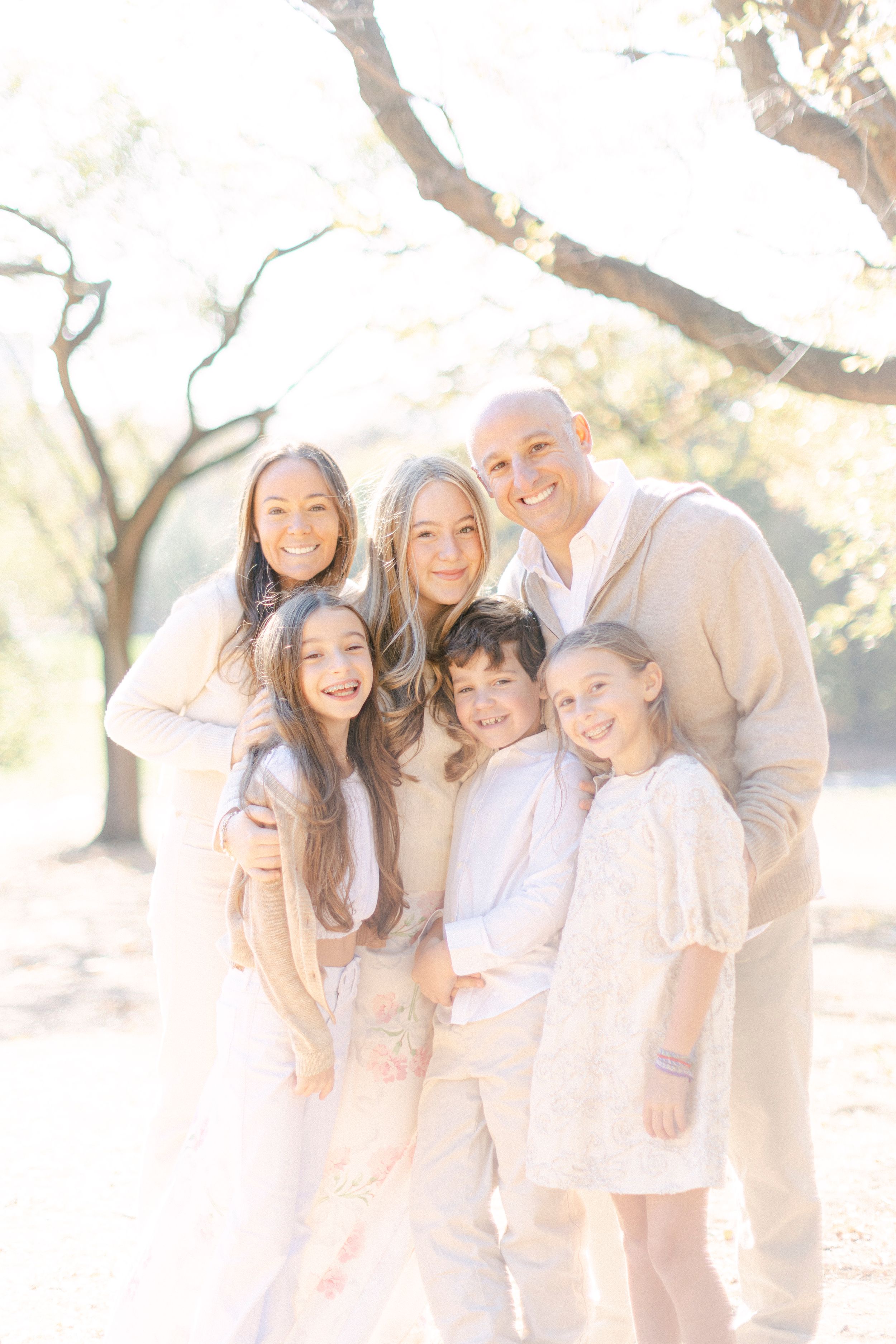 Family group portrait outdoors in coordinated cream and white outfits with ethereal lighting.