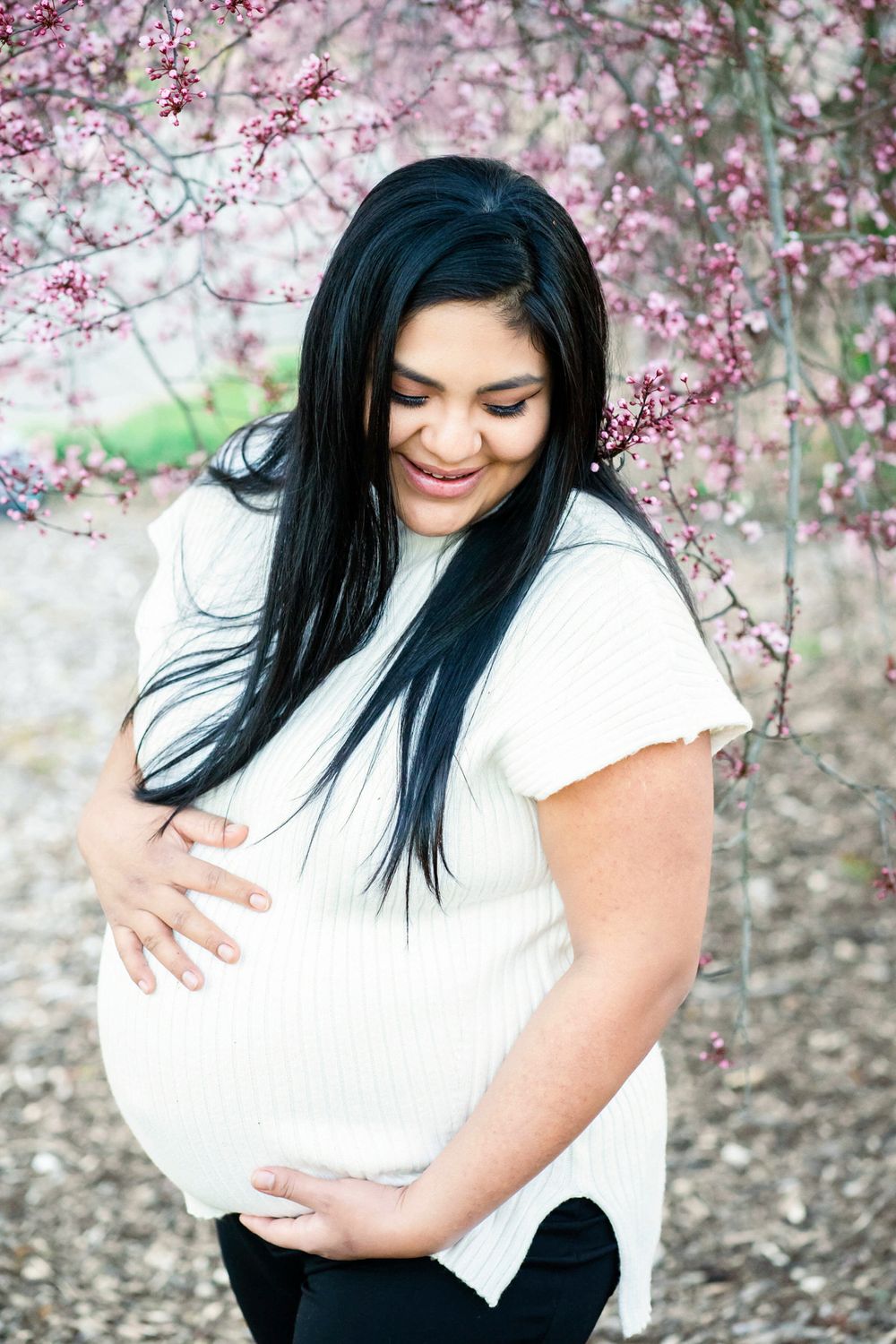 maternity portrait of a young mom wearing white and standing by pink blossoms