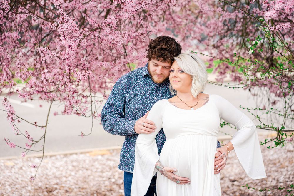maternity portrait of mom and dad embracing by a pink floral tree
