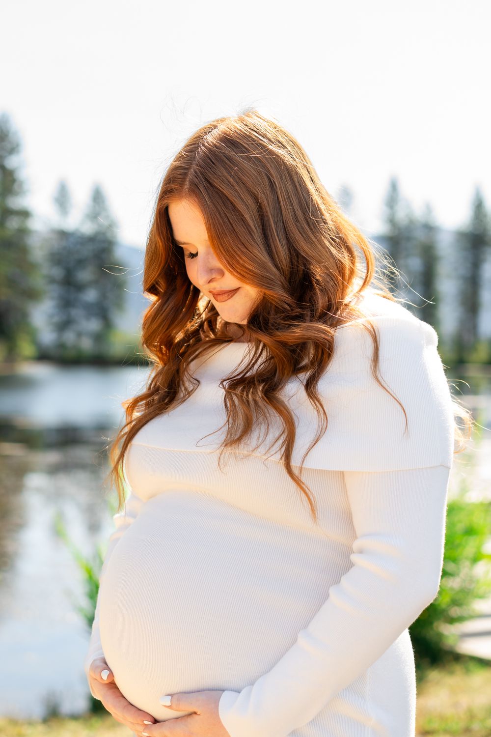 Maternity portrait of mom dressed in white and looking down at baby bump