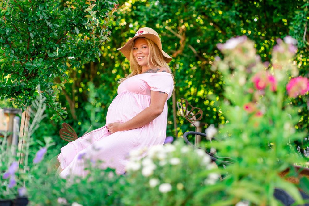 maternity portrait of mom in a pink dress sitting on a tractor in a flower garden