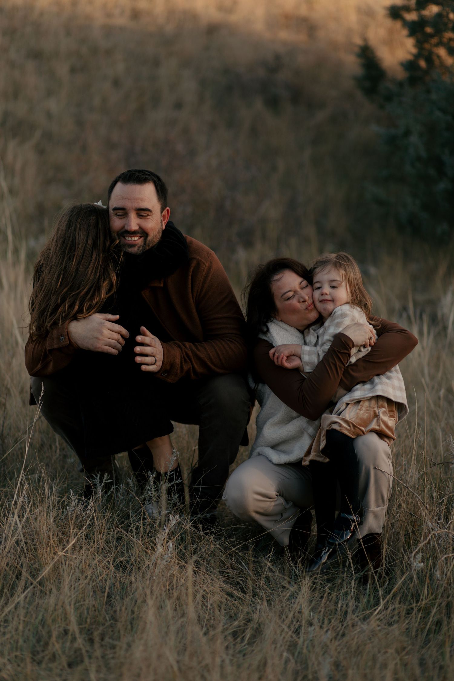 An intimate family portrait shows warm embraces and smiles while kneeling in tall autumn grass.