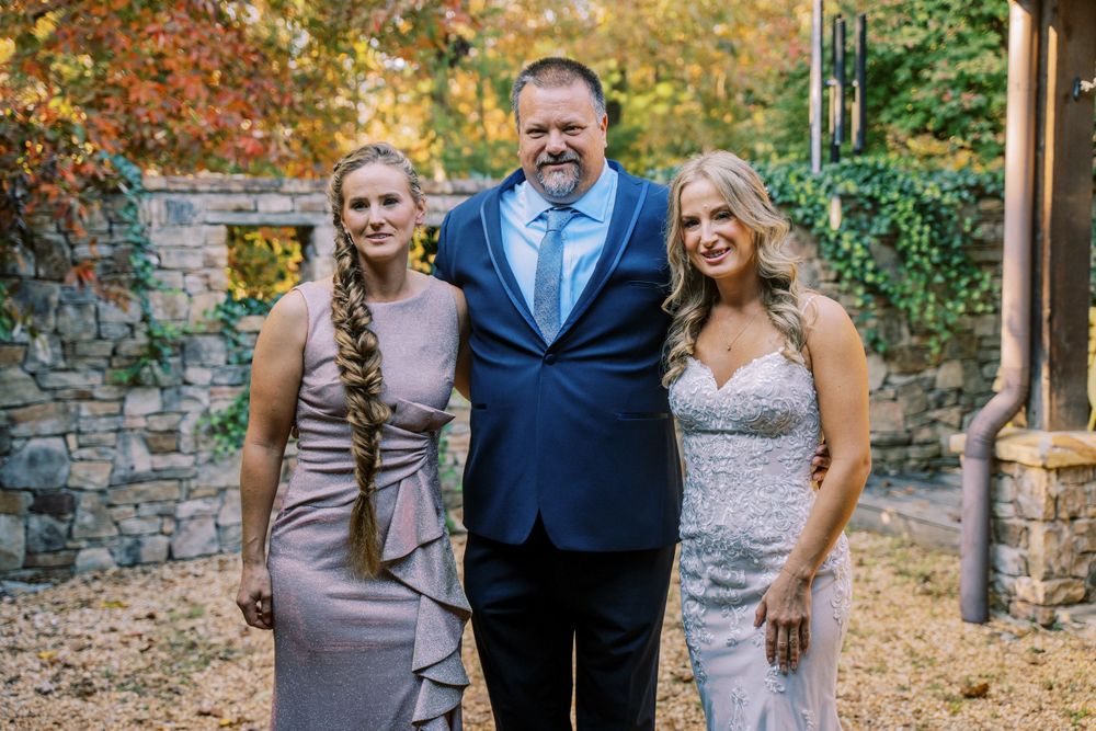 Wedding party members pose together against a stone wall backdrop during fall.