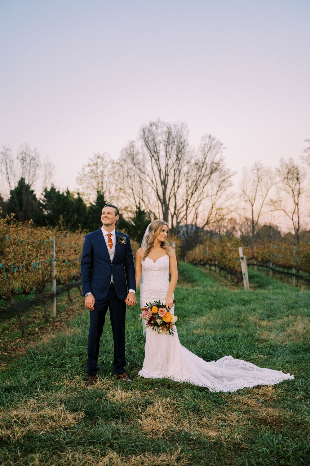 Newlyweds pose in a vineyard with fall foliage and long flowing wedding dress.