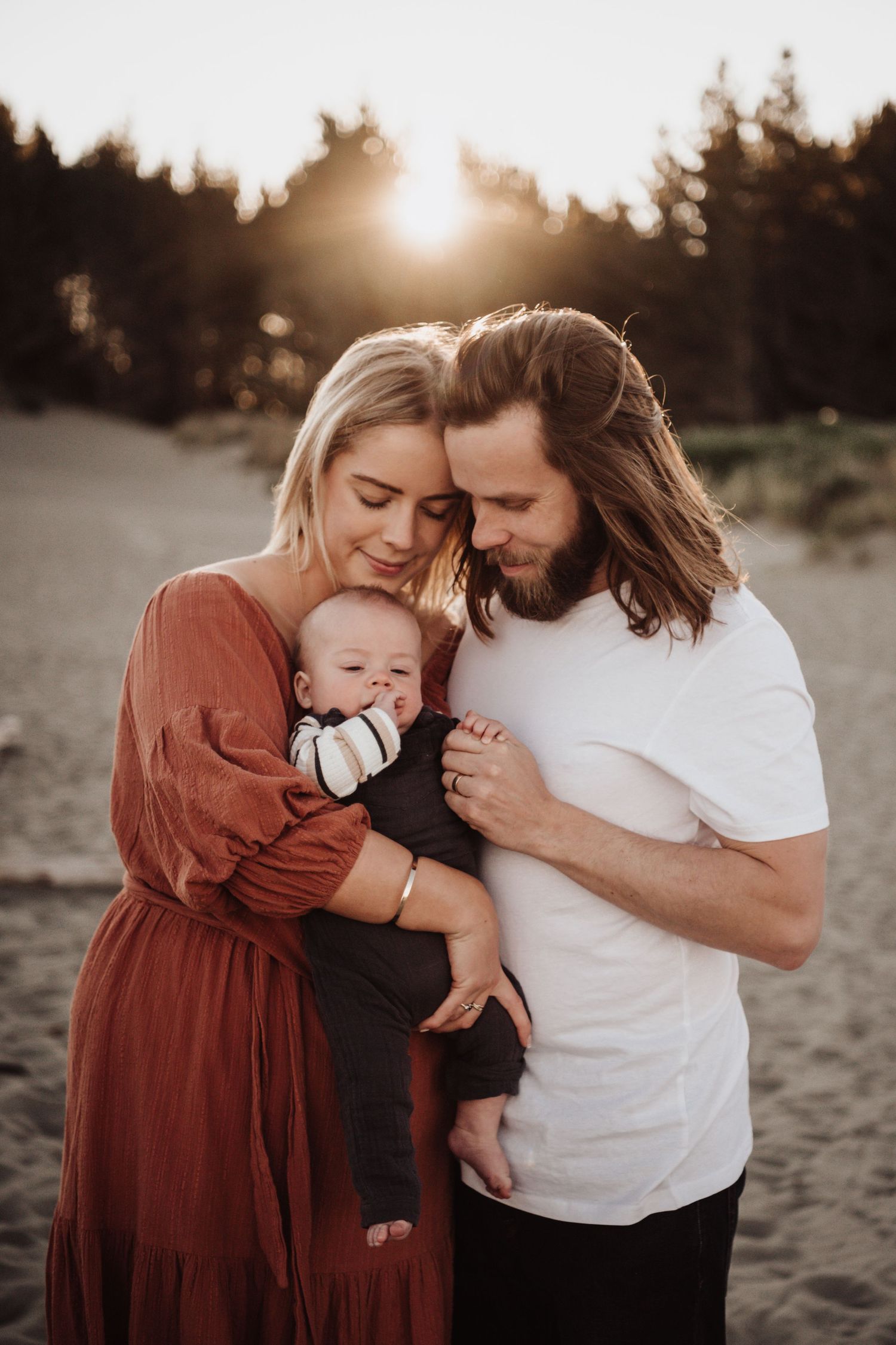 Family shares tender moment together at sunset on sandy beach.