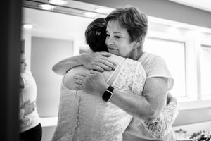 Two women share a heartfelt embrace in a black and white wedding preparation photo.