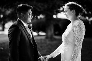Black and white portrait of bride and groom holding hands and gazing at each other outdoors.