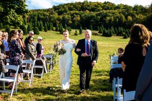 Bride walks down the outdoor aisle escorted by her father at a scenic farm wedding ceremony.